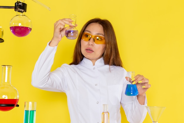 Foto grátis vista frontal do jovem feman químico em terno branco na frente da mesa trabalhando com soluções