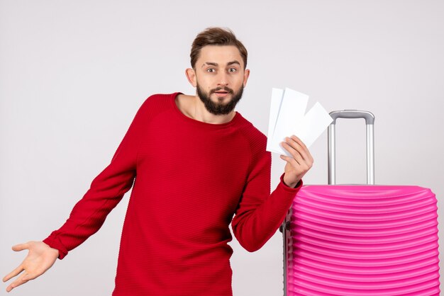 Vista frontal do jovem homem com bolsa rosa e segurando os bilhetes na cor branca da cor viagem férias voo viagem turista
