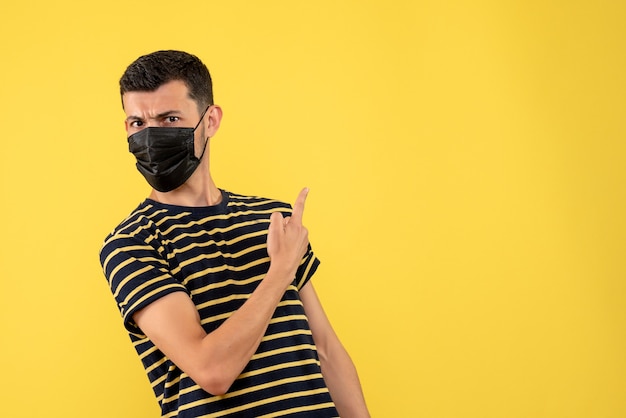 Foto grátis vista frontal do jovem homem com camiseta listrada em preto e branco apontando para as costas em fundo amarelo