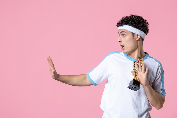 Foto grátis vista frontal do jovem jogador com roupas esportivas com copo dourado na parede rosa
