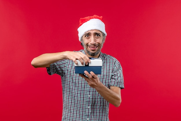 Vista frontal do jovem macho abrindo o presente de Natal no vermelho