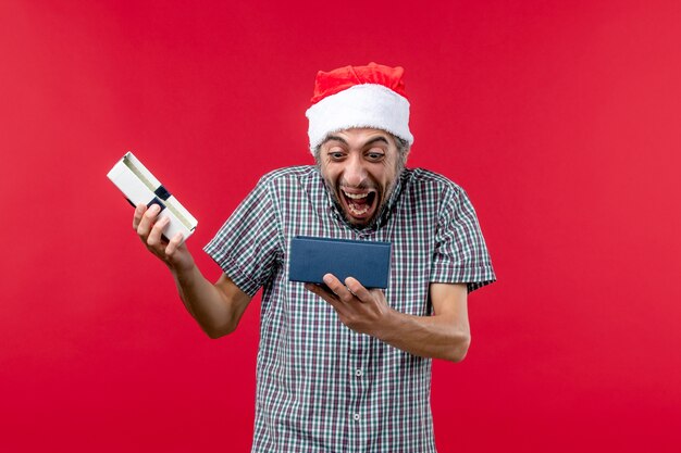 Vista frontal do jovem macho abrindo o presente de natal no vermelho