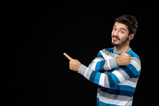 Vista frontal do jovem macho em camisa listrada azul na parede preta