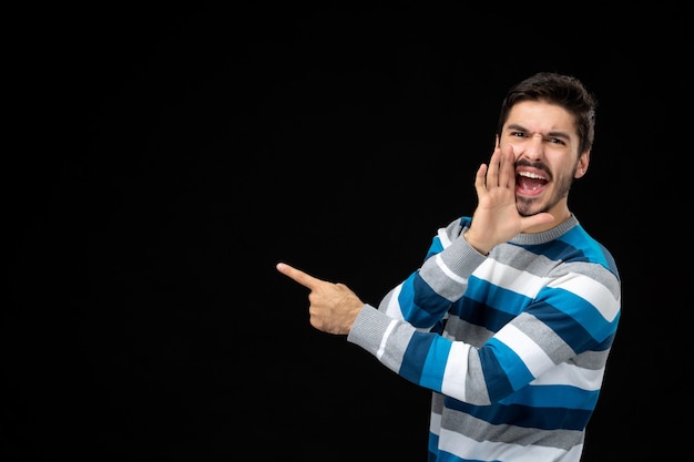 Vista frontal do jovem macho em camisa listrada azul na parede preta