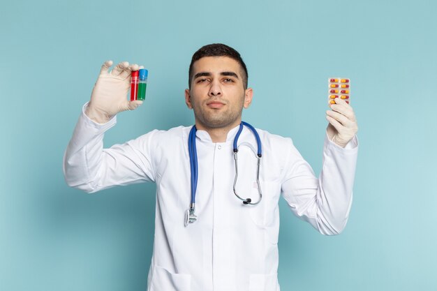 Vista frontal do jovem médico de terno branco com estetoscópio azul segurando frascos