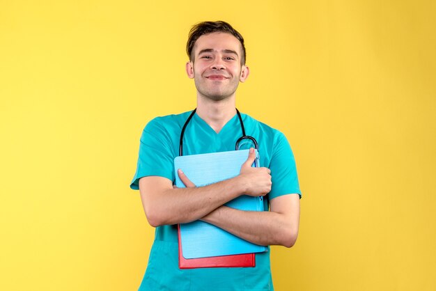 Vista frontal do jovem médico segurando análises na parede amarela