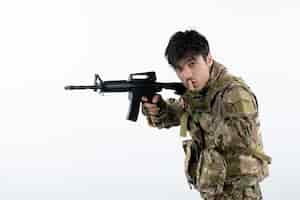 Foto grátis vista frontal do jovem soldado camuflado com metralhadora parede branca
