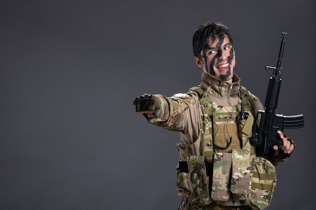 Vista frontal do jovem soldado camuflado com parede escura de metralhadora