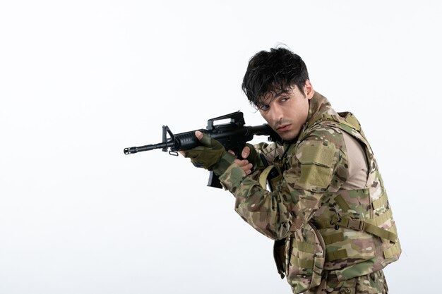 Vista frontal do jovem soldado lutando camuflado com metralhadora parede branca