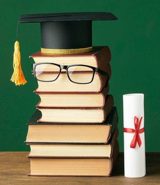 Vista frontal do livro empilhado com boné acadêmico e óculos