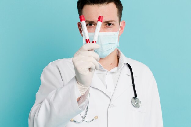 Vista frontal do médico com máscara médica segurando vacutainers