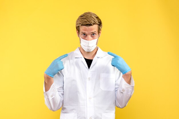Vista frontal do médico com máscara sobre fundo amarelo covida - pandemia de saúde médica