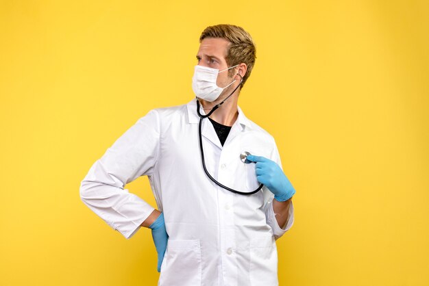 Vista frontal do médico com máscara sobre vírus de fundo amarelo, pandemia de saúde covid