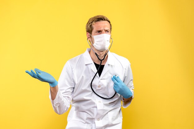 Vista frontal do médico com máscara sobre vírus de fundo amarelo, pandemia de saúde covid