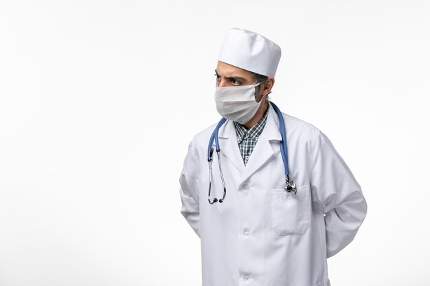 Foto grátis vista frontal do médico do sexo masculino em traje médico e máscara devido a coronavírus em doença de isolamento de piso branco covid- vírus pandêmico