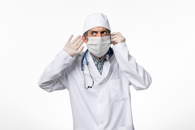 Vista frontal do médico em terno branco e máscara devido a coronavírus na superfície branca