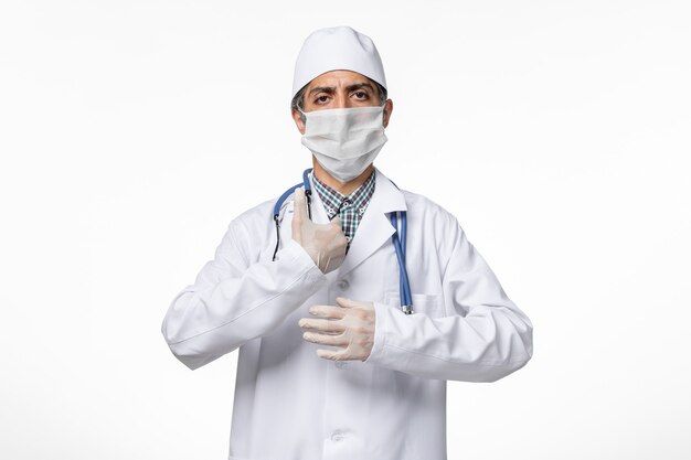 Vista frontal do médico em terno médico com máscara devido a coronavírus na superfície branca