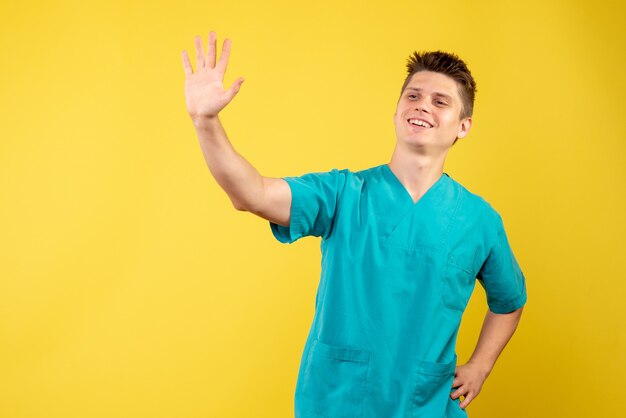 Vista frontal do médico em terno médico, saudação na parede amarela