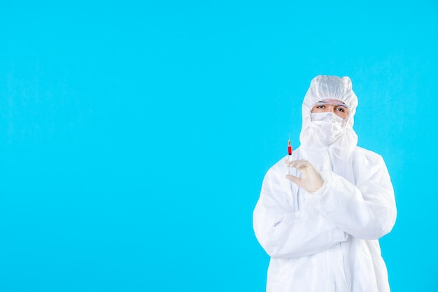 Vista frontal do médico em traje de proteção segurando injeção no azul