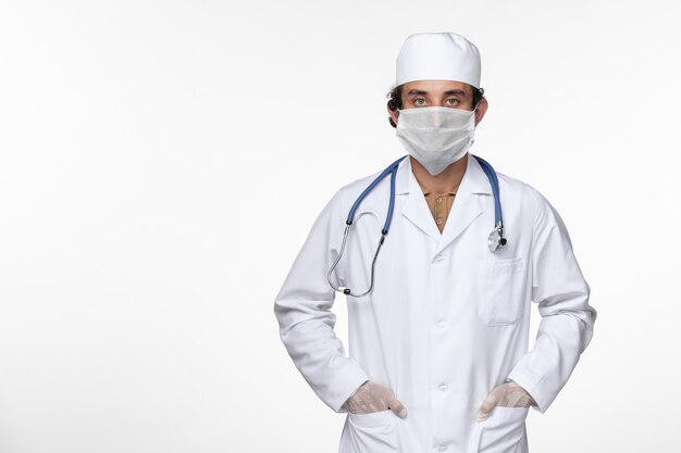 Vista frontal do médico em traje médico usando máscara esterilizada como proteção contra a doença pandêmica de coronavírus do vírus da mesa branca