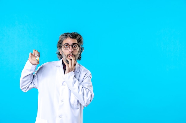 Foto grátis vista frontal do médico em uniforme médico segurando o pequeno frasco no azul