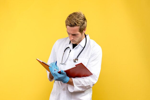 Vista frontal do médico escrevendo notas sobre fundo amarelo vírus saúde médico humano