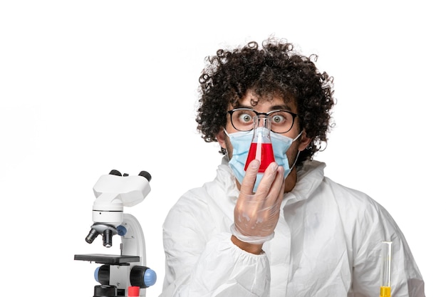 Foto grátis vista frontal do médico masculino com traje de proteção e máscara segurando o frasco com solução vermelha sobre fundo branco.