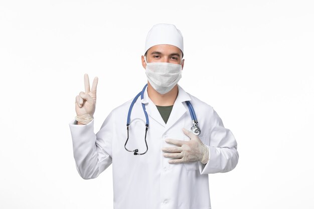 Vista frontal do médico masculino com traje médico e máscara devido a covid- on light desk disease virus covid- doença