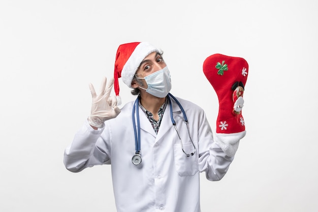 Vista frontal do médico masculino com uma grande meia de férias na parede branca vírus covid - natal