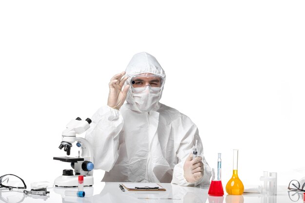 Vista frontal do médico masculino em traje de proteção com máscara devido a uma injeção secreta no espaço em branco claro