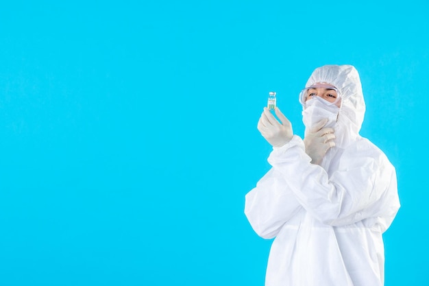 Vista frontal do médico masculino em traje de proteção e máscara segurando um pequeno frasco em azul