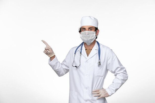 Vista frontal do médico masculino em traje médico usando máscara como proteção contra covid- on the white floor, doença, saúde, covidemia