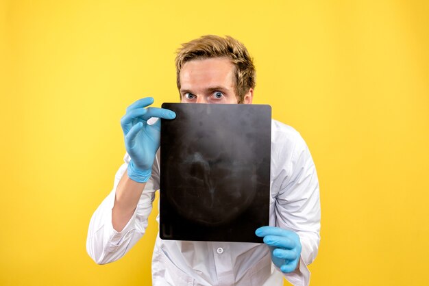 Foto grátis vista frontal do médico segurando um raio-x em fundo amarelo médico cirurgia higiene covid