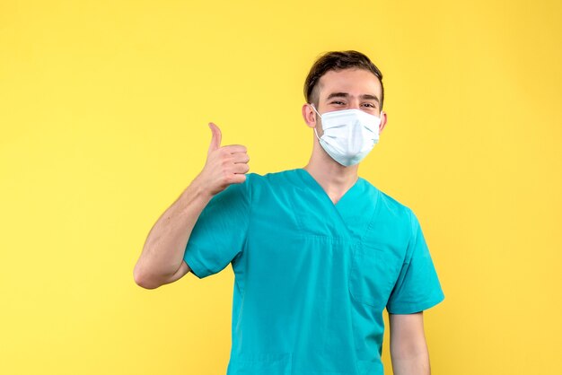 Vista frontal do médico sorrindo com máscara na parede amarela