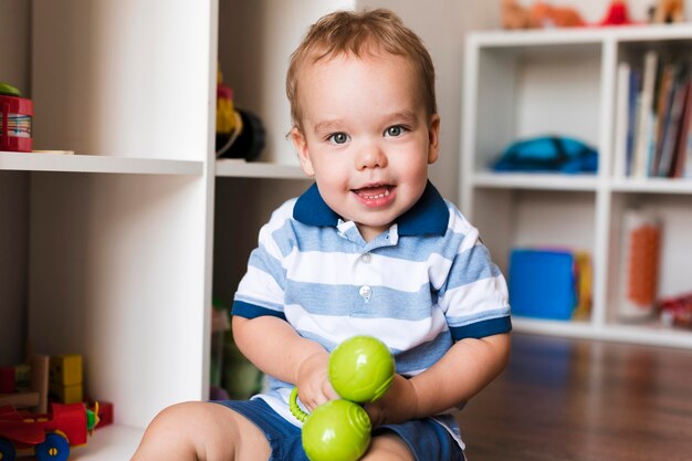 Vista frontal do menino feliz e fofo brincando com brinquedos