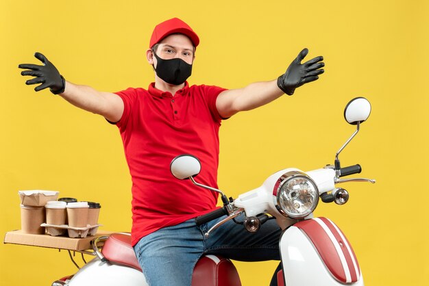 Vista frontal do mensageiro usando blusa vermelha e luvas com máscara médica, entregando pedidos sentado na scooter, estendendo os braços para a frente