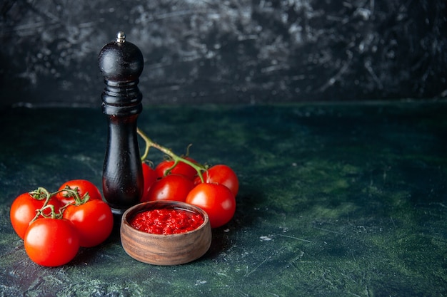 Vista frontal do molho de tomate com tomates vermelhos frescos na superfície escura de cor vermelha temperando sal pimenta