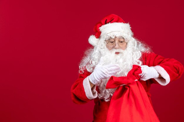 Vista frontal do papai noel abrindo uma sacola cheia de presentes para as crianças em um feriado vermelho natal emoção
