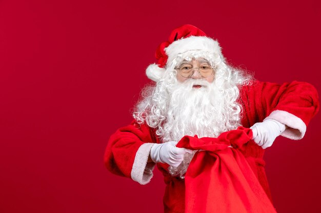 Vista frontal do papai noel abrindo uma sacola cheia de presentes para as crianças na mesa vermelha feriado natal emoção
