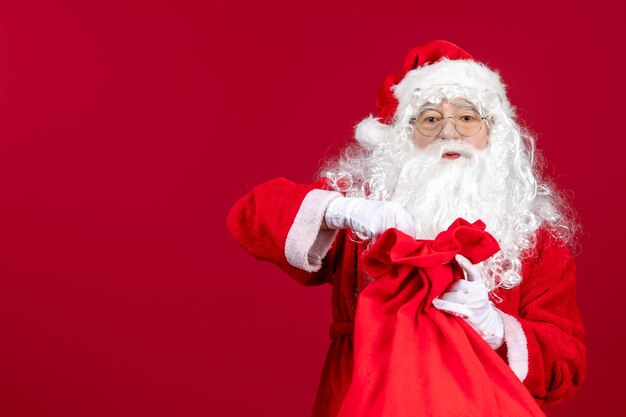 Vista frontal do papai noel abrindo uma sacola vermelha cheia de presentes para as crianças em um feriado vermelho natal emoção