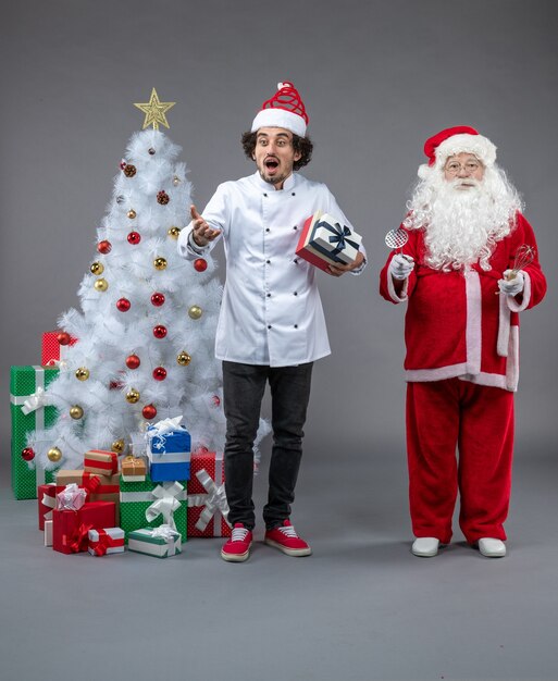 Vista frontal do Papai Noel com cozinheiro e presentes de Natal na parede cinza