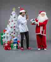 Foto grátis vista frontal do papai noel com cozinheiro masculino em volta dos presentes de natal na parede cinza