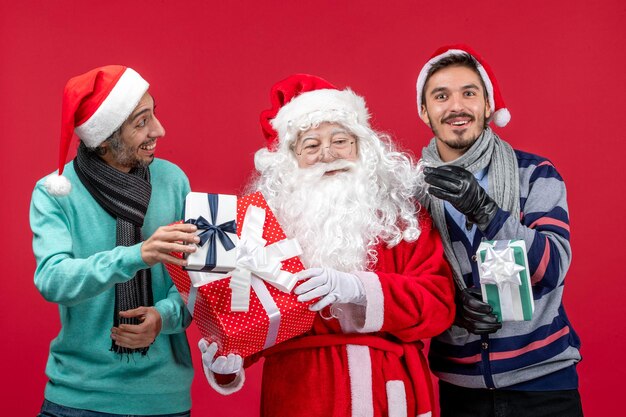 Vista frontal do papai noel com dois homens segurando presentes em uma emoção de presente de ano novo vermelho vermelho Natal