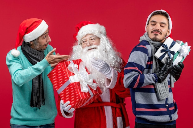 Vista frontal do papai noel com dois homens segurando presentes na emoção vermelha presente de ano novo vermelho