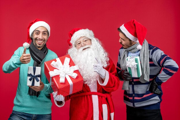 Vista frontal do papai noel com dois homens segurando presentes no vermelho, emoções do presente de ano novo vermelho de natal