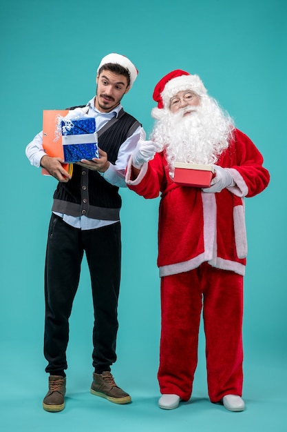 Vista frontal do papai noel com jovem macho e presentes na parede azul