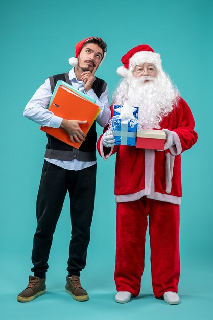 Vista frontal do Papai Noel com jovem macho e presentes na parede azul