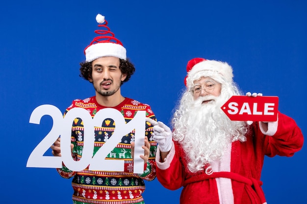 Vista frontal do papai noel com jovem segurando e escritos de venda na cor azul da neve ano novo natal