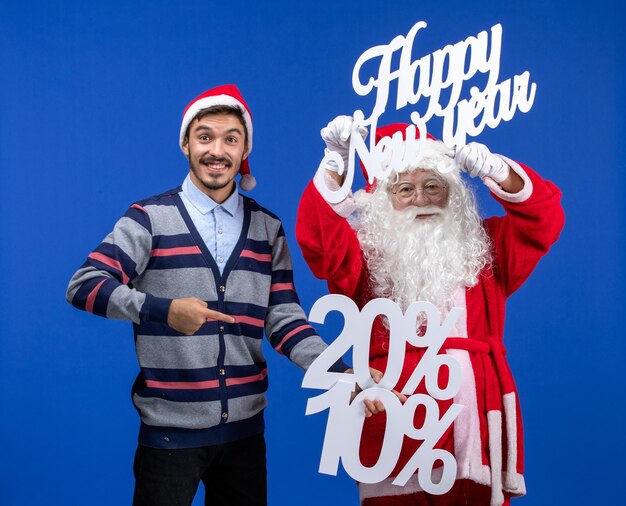 Vista frontal do papai noel com jovem segurando feliz ano novo e números escritos na parede azul