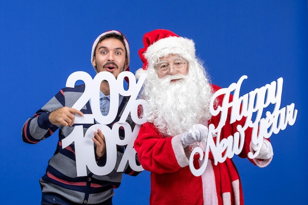 Vista frontal do papai noel com jovem segurando feliz ano novo e números escritos na parede azul